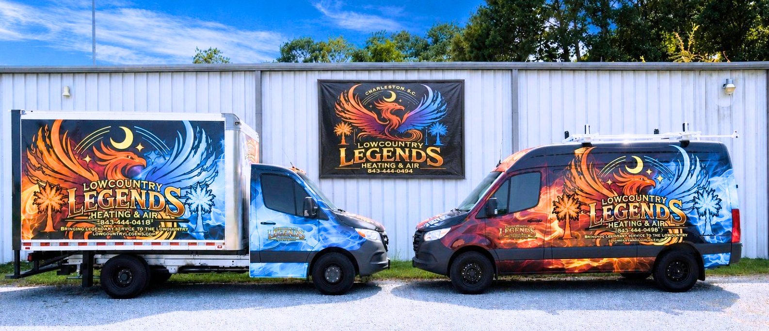 Two vehicles from Lowcountry Legends Heating & Air, one a box truck and the other a van, parked side by side against a backdrop of a company sign. The vehicles feature vibrant, colorful designs with phoenix and palm tree motifs.